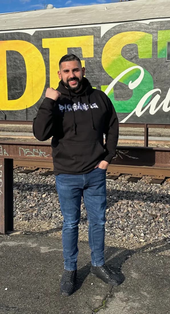 Daniel in the Dead Prezident hoodie in front of a painted mural by the train tracks.