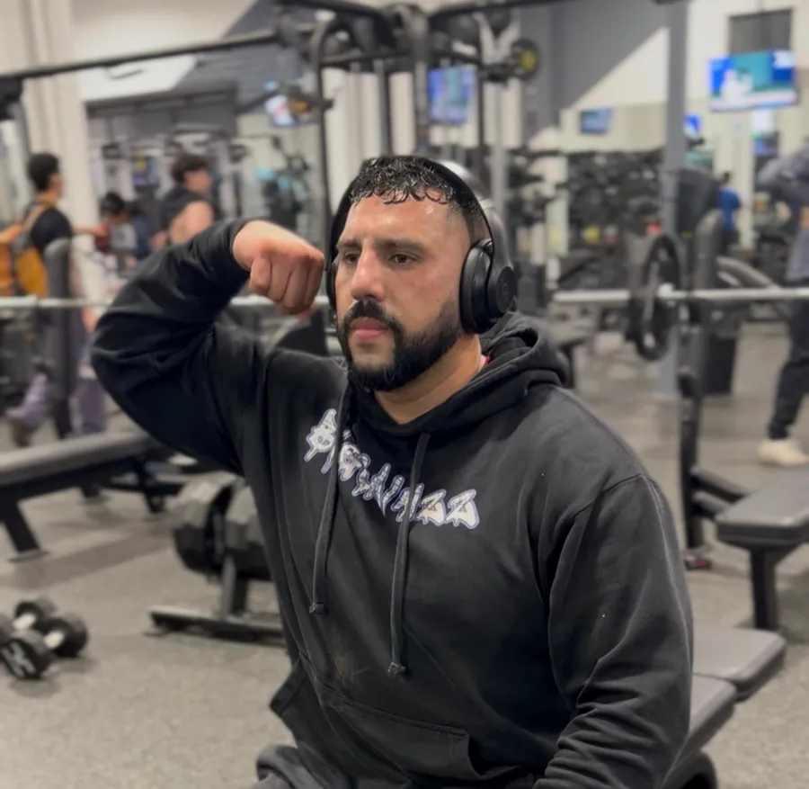 Daniel in a black BIGGAINZZ hoodie and headphones, flexing between sets at the gym.